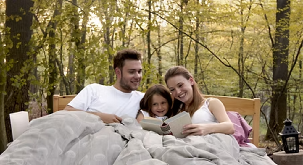 Drei Personen lesen gemeinsam im Bett im Wald